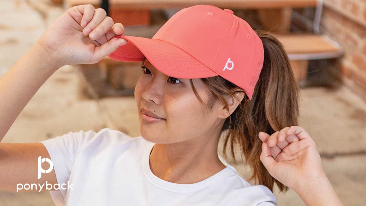 Woman wearing a coral Ponyback Ponytail hat and a white t-shirt