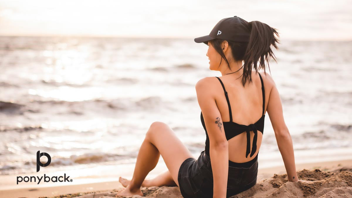 Woman wearing black Ponyback ponytail hat on the beach at sunset