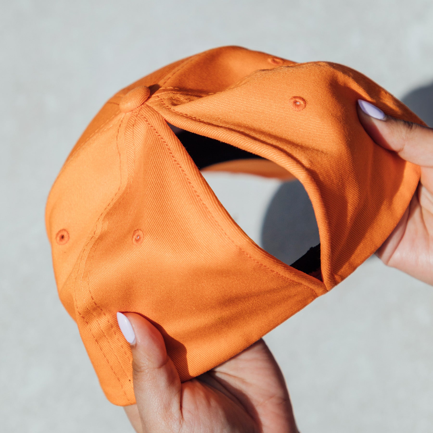 Person holding an orange Everyday Fit Apricot Crush baseball cap against a concrete background.